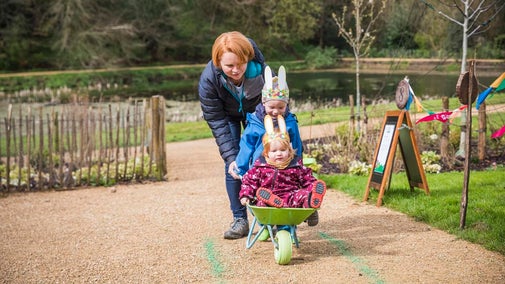 A mother and two children enjoying a wheelbarrow race at Prior Park for Easter
